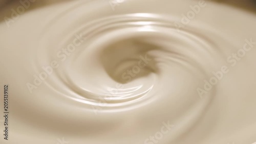 Creamy mixture swirling in a bowl, showing continuous motion and texture as it blends, with a smooth surface and subtle reflections in the light