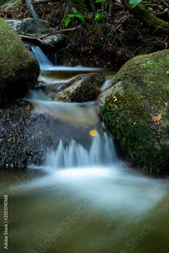 Stream water cascading over mossy rocks in a forest, creating a tranquil, natural environment with blurred motion