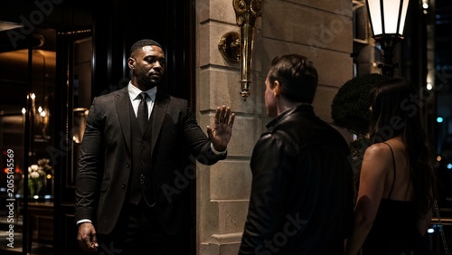 doorman. Club entrance with doorman gesturing refusal, night atmosphere, architectural details, social commentary. real-estate listings.