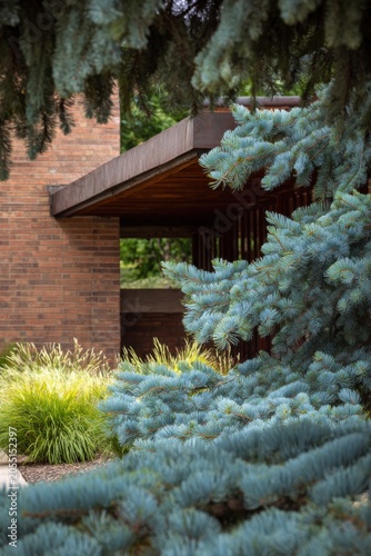 Lush green plants elegantly encircle a contemporary brick structure adorned with wooden accents, all set in a bright and sunny outdoor atmosphere during the day