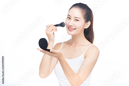 Obraz na plátně Smiling young woman applying makeup with brush and compact mirror on white