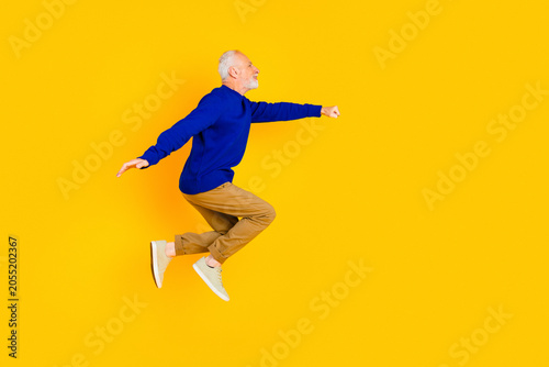 Active senior man jumping joyfully against a bright yellow background wearing a blue sweater and casual sneakers for fitness  energy and positive lifestyle imagery