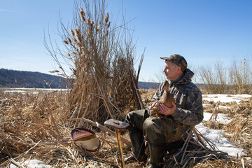 A hunter with a decoy duck sits next to his duck blind