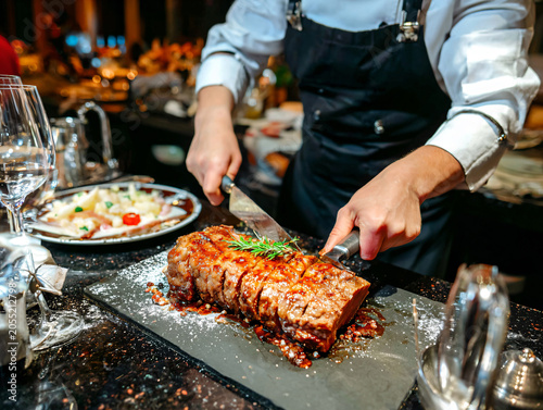 A chef is carving picanha steak juicy slices with fire and smoke in the background.