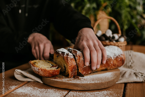 Close-up of baker hands slicing a fresh homemade sweet pastry roll with a knife on a wooden board, rustic food styling.