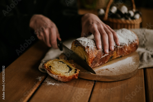 Close-up of baker hands slicing a fresh homemade sweet pastry roll with a knife on a wooden board, rustic food styling.