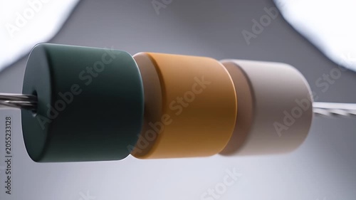 Close-up shot of three colorful cylindrical beads threaded on a thin wire against a soft blurred background