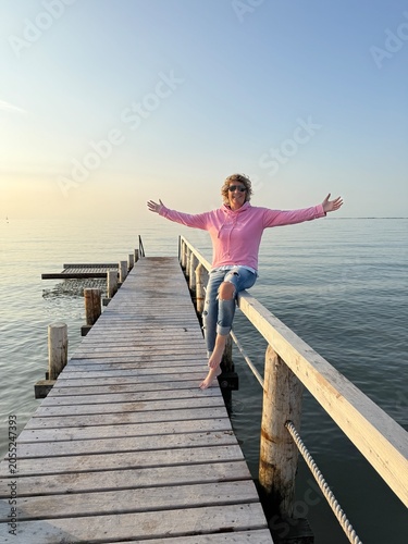 cheerful young woman sits on a wooden pier at the beach during summer vacation