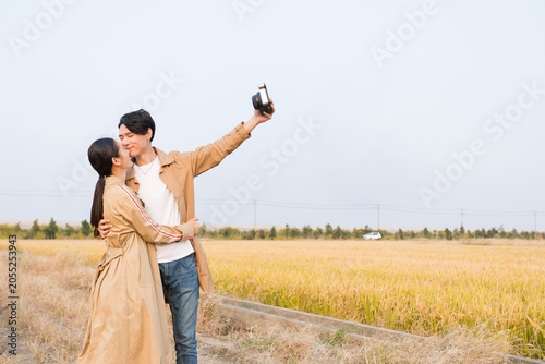 Bild auf Leinwand Romantic young couple embracing and taking a self portrait in a golden field