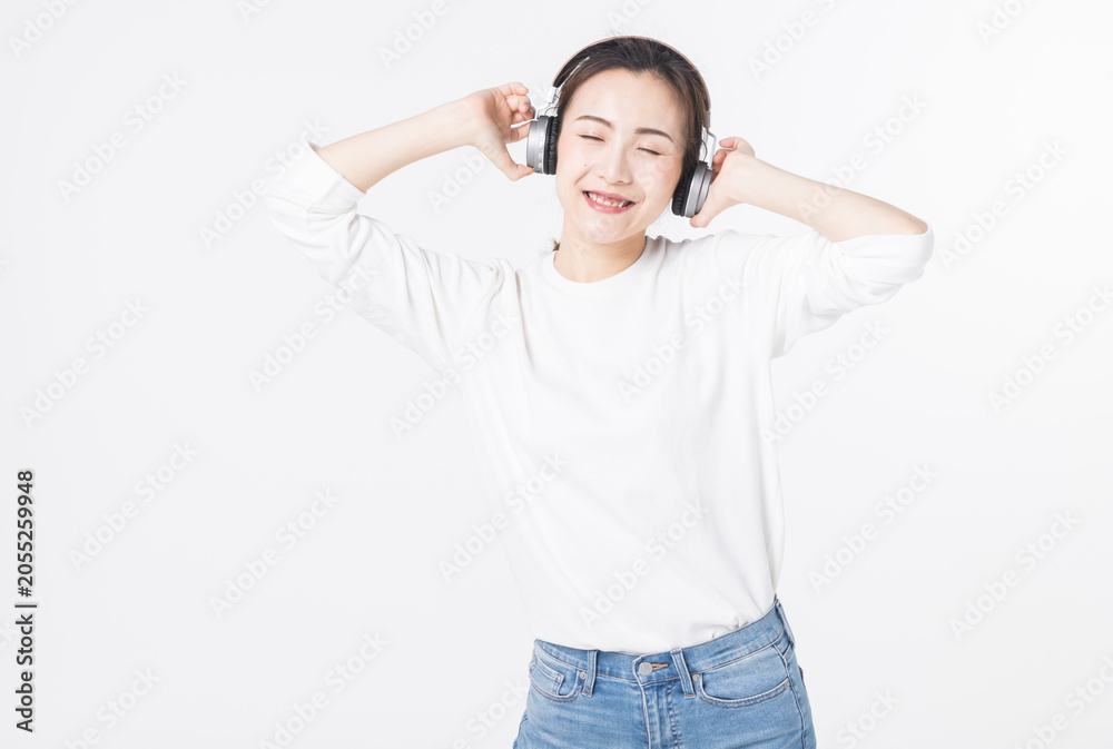 Fototapeta premium Happy young woman listening to music with headphones on light background