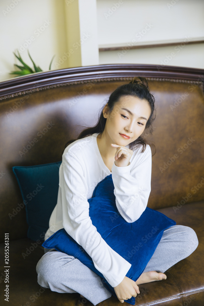 Fototapeta premium Relaxed young woman sitting on sofa with blue cushion at home