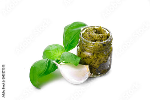 Green pesto sauce in a small glass jar isolated on white background. Traditional Italian basil pesto with garlic clove, top view close up.