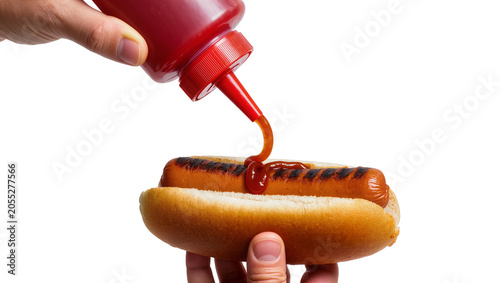 Фотография Isolated hand squeezing red ketchup bottle onto a grilled hot dog in a bun