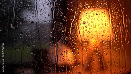 Close-up macro view of rain drops on a window with warm orange light glowing behind