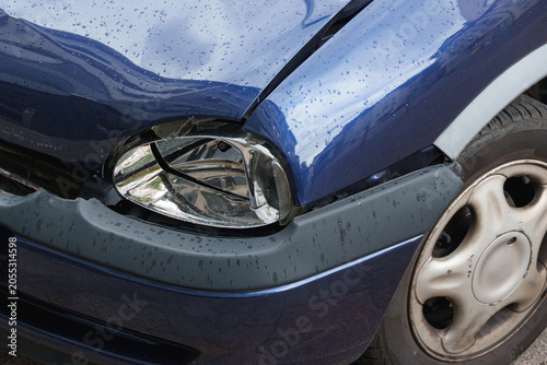 Damaged blue car front with broken headlight after traffic collision incident