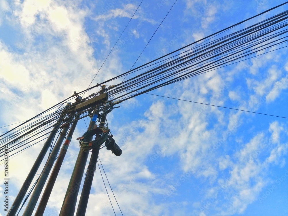 Fototapeta premium Utility poles with tangled electrical wires and cables against a blue cloudy sky