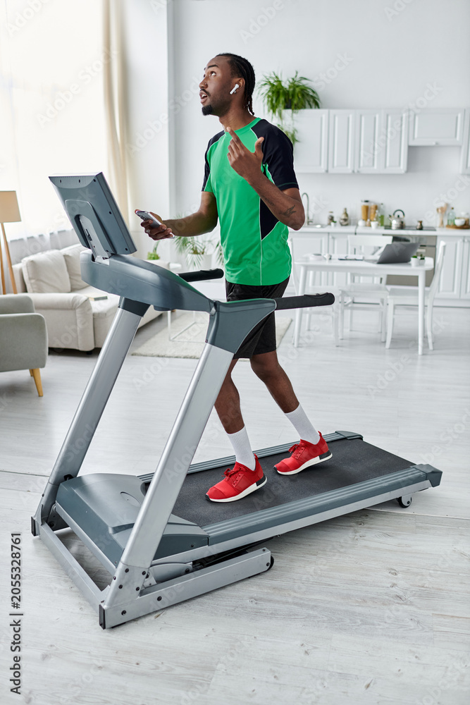 Fototapeta premium Young african american man embraces fitness while using earphones at home in a modern and stylish space