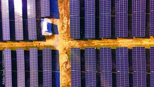 Overhead solar modules at crossroads of service paths. Aerial view of blue photovoltaic panels around an earth-tone intersection with a small white structure.