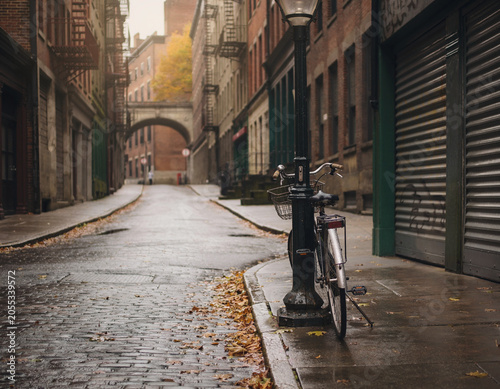 A lone bicycle keeps watch beside a streetlamp on a rain-slick alley, as the city holds its breath