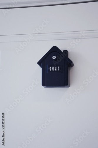 A wall mounted black key lock box with a combination lock mounted above a traditional keyhole on a white door