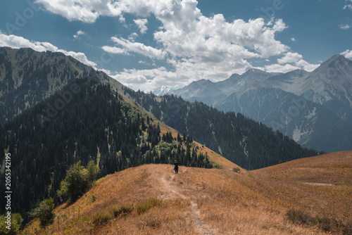 A lonely hiker walks on a dirt trail through mountain ridges near Almaty, Kazakhstan. Neutral landscape background with copy space for travel, active lifestyle, and adventure concepts.