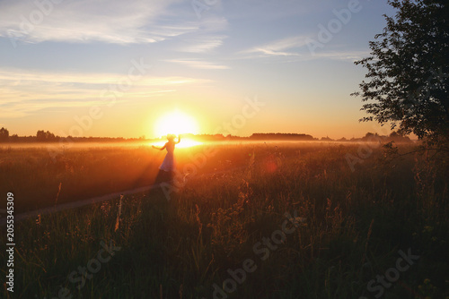 Silhouette of a girl dancing in a field at dawn in the fog