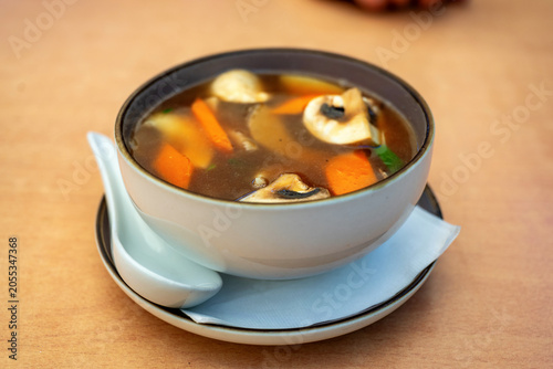 Asian mushroom and vegetable spicy soup in bowl and plate on table.