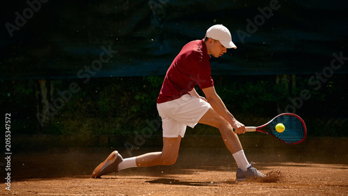 Schilderij op canvas Tennis player reaching low ball with backhand on dusty clay court