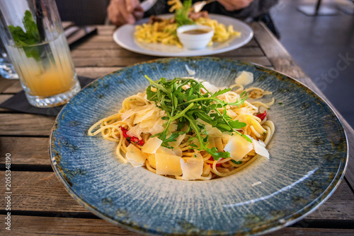 Spaghetti aglio olio pepperoncino with parmesan and arugula leaf on blue plate.