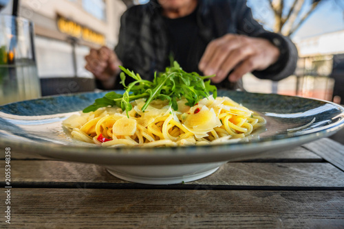 Man (part of) eating spaghetti aglio olio pepperoncino in outdoor restaurant.