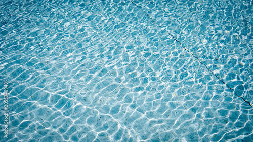 Clear blue swimming pool water surface with ripples and sunlight reflection.