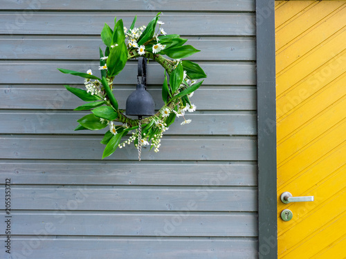 Spring floral wreath with fresh green leaves and white wildflowers hanging on a modern gray wooden wall beside a bright yellow door