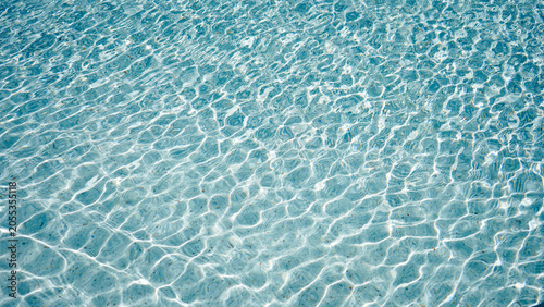 Clear light blue swimming pool water surface with ripples and sunlight reflection.