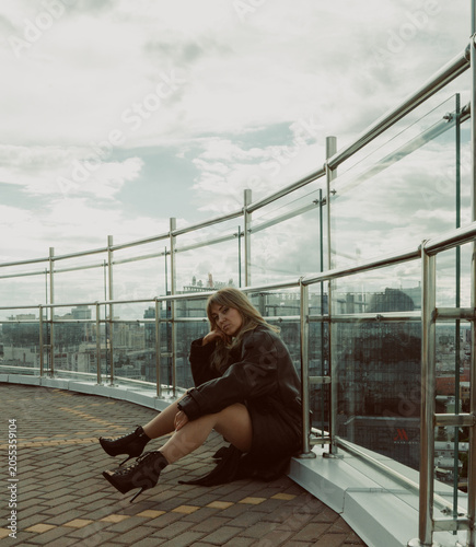 A girl in a black cloak poses on the roof of a building in the city