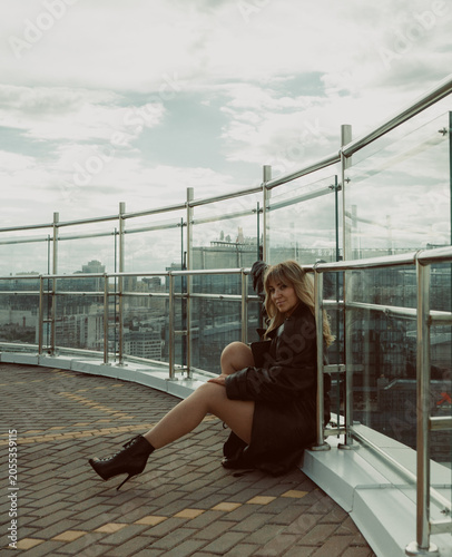 A girl in a black cloak poses on the roof of a building in the city