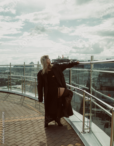 A girl in a black cloak poses on the roof of a building in the city