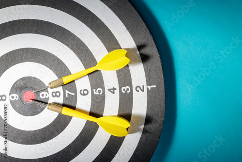 Fotografie A top-down close-up view of a dartboard where two yellow flights darts have accurately pierced the red bullseye circle, signifying ultimate business success, accuracy, and goal achievement