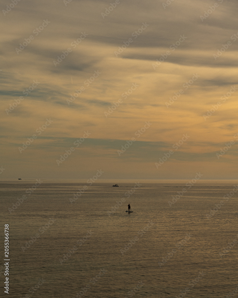 Fototapeta premium Lone paddleboarder on a calm golden sea at sunset under a vast sky, Mediterranean, Mallorca