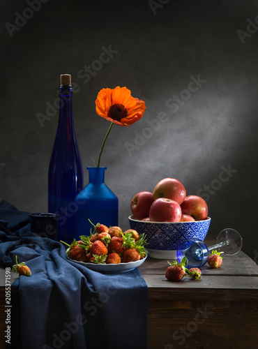 Still life with red apples, strawberries, red poppy seeds in a blue bowl on a dark background