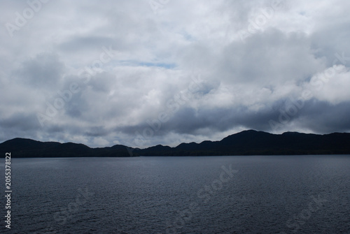 Clouds covered sky, ocean in the foreground, and Alaska's coast on the horizon