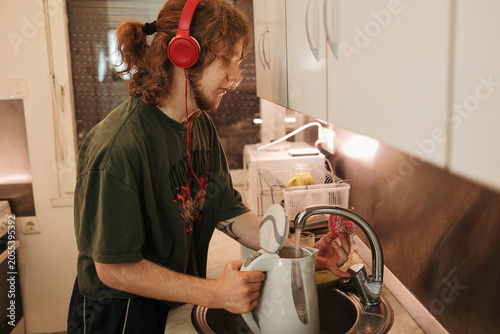Young man filling an electric kettle with water while preparing a hot drink at home. Concept of beverage preparation, household routine, independence and everyday life.