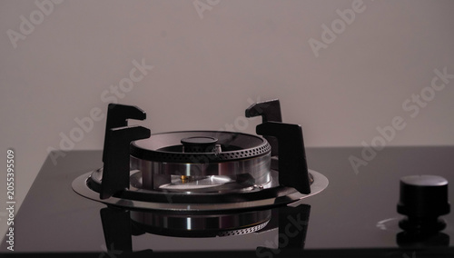 Close-up of a modern gas stove burner on a black glass cooktop. The sleek stainless steel design highlights contemporary kitchen appliances and cooking technology.