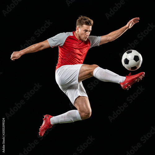 Dynamic Soccer Player Jumping and Kicking Ball in Mid Air Isolated on Black Background