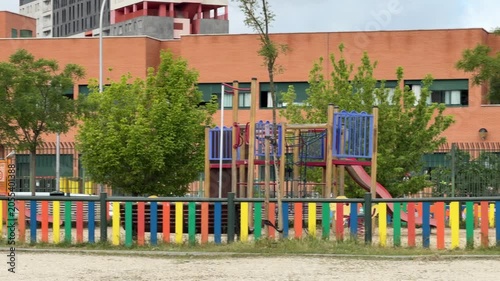 Madrid, Spain, June 9-2026: View of a school playground with colorful fence, play equipment, trees, and modern educational buildings in an urban environment. Exterior scene on a cloudy day.