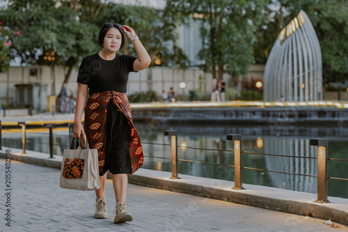 Canvastavla Shopaholic fashionable adult Asian woman walking on the city street and holds a shopping bag