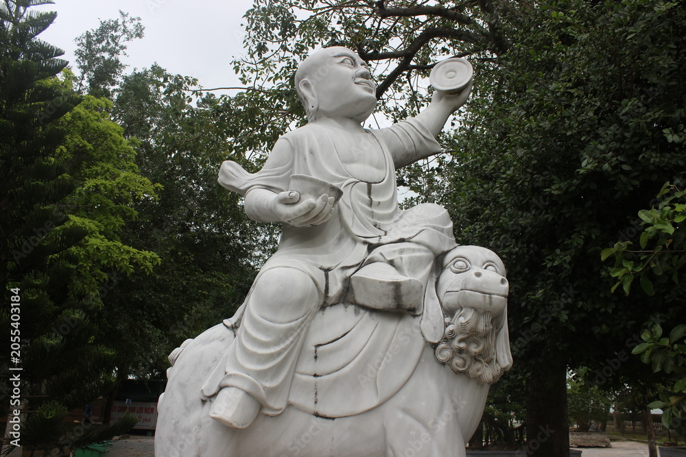Obraz premium Marble statue of monk riding mythical beast in sunny tropical garden of temple site.