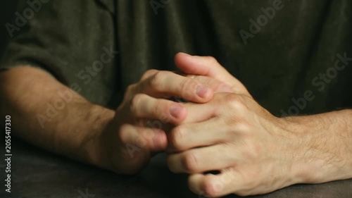 Close up nervous man wringing hands on dark table, showcasing anxiety, stress, and inner turmoil through restless and agitated body language while sitting alone. Anxious man rubbing and wringing hands