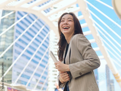 Confident young Asian businesswoman smiling outdoors in a modern urban environment with office buildings in the background.