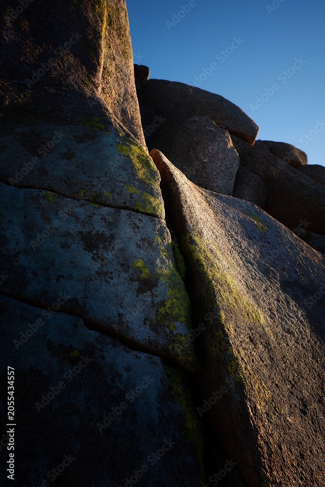 Fototapeta premium Rugged Mountain Rock Formation with Lichen and Clear Blue Sky at Sunset