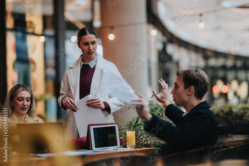 Photography Three business colleagues review papers and argue over work at an outdoor cafe table
